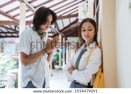 boy with headphones gesture apologizes to a girl in high school uniform who got angry Royalty-Free Stock Photo #1934479091