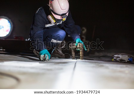Male worker test steel tank butt weld overlay carbon bottom plate of storage tank oil background white contrast of magnetic field test