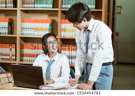 male and female high school students chat by studying together with a pile of books and a laptop on a table