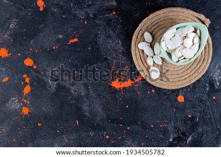 On navy blue background with orange spot, pumpkin seeds in sky blue bowl. High quality photo