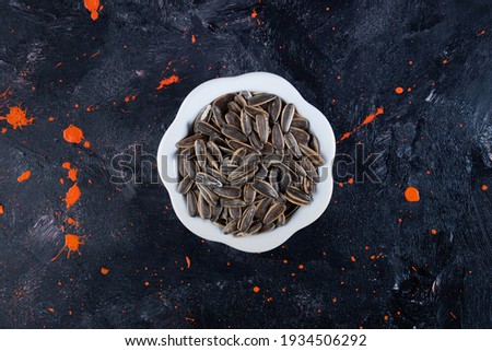 In navy blue table with orange spots, vintage white bowl with sunflower seeds. High quality photo