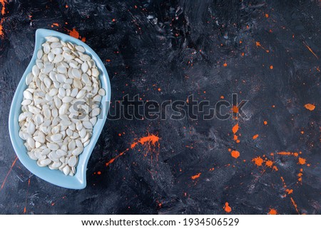 Isolated on dark colored background, sky blue plate with pumpkin seeds. High quality photo