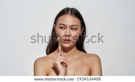 Young girl looking to the side while standing in the studio. Brunette with skin care roller. Self-care and youth and beauty support concept. Cosmetic products for female