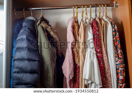 Separation of the wardrobe for summer and winter. Clothes on hangers in dark and light colors