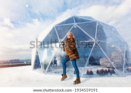 Girl beside An unusual round, glass house in the style of eco-architecture. Winter house. Light architectural structure with a natural silhouette, stained glass decoration.