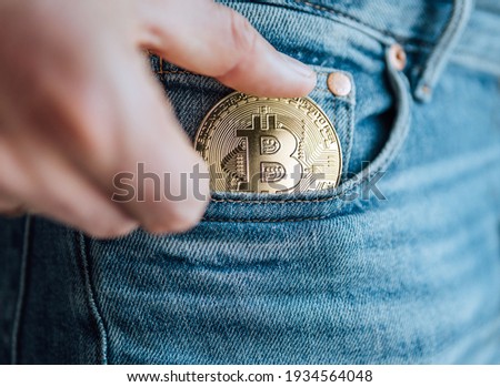 Close up footage of man's fingers putting the Bitcoin coin in the blue jeans small pocket. Savings, digital currency, cryptocurrency, investing, and smart outgoings managing concept.