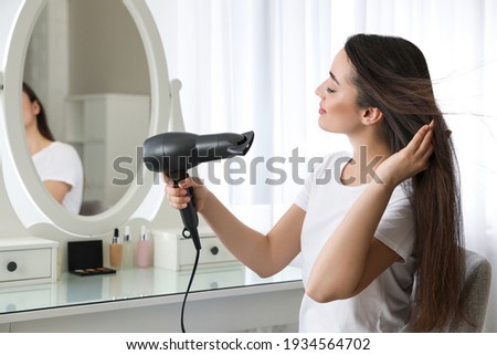 Beautiful young woman using hair dryer near mirror at home Royalty-Free Stock Photo #1934564702
