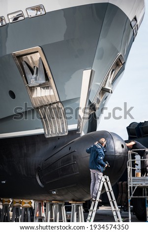 Super yacht crew working on the bow of a hauled out superyacht with steps and scaffolding during yard service and winter maintenance  Royalty-Free Stock Photo #1934574350