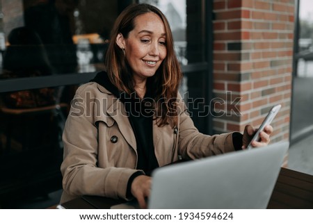 business focused confident successful freelancer adult woman blogger works using technology laptop phone communicates performs tasks studies in the workplace office in a public place in a coffee shop