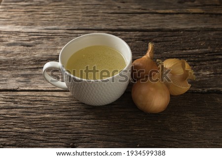 Bowl with clear, rich broth. White crockery on a wooden table at the age. Bow about a mug