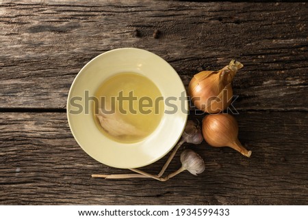 Bowl with clear rich broth. White crockery on an aged wooden table. Vegetables - onions, garlic, spices