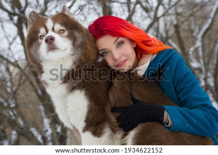 Close-up portrait of young girl hugging her husky dog in winter park. Beautiful girl in warm jacket and hat play in a winter park with a dog on a walk. Winter background. 
Outdoor winter activities