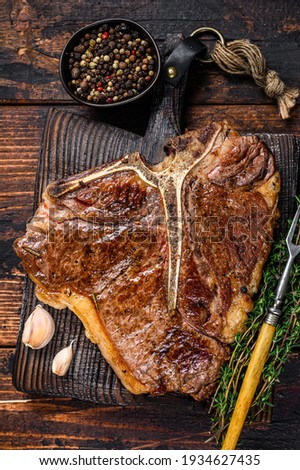 Roast t-bone or porterhouse beef meat Steak on a wooden cutting board. Dark wooden background. Top view.