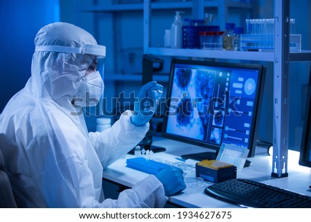 Doctor in protective suit is doing a science experiments and developing vaccine in a modern laboratory. Genetic engineers workplace. The concept of science and medicine. Royalty-Free Stock Photo #1934627675