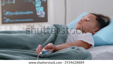 Little afro boy sleeping in hospital bed attached to monitors. Portrait of unconscious preteen kid patient with oximeter on finger lying in bed in intensive care unit