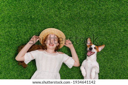 Laughing girl and cute dog enjoy summer day on the grass in the park. Spring, Easter background. Top view portrait. Royalty-Free Stock Photo #1934641142