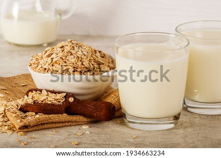 Oatmeal in a white bowl with a glass of milk on a white blue background. A healthy, nutritious morning breakfast. Oat milk. Healthy vegan non-dairy organic drink with flakes.  Royalty-Free Stock Photo #1934663234