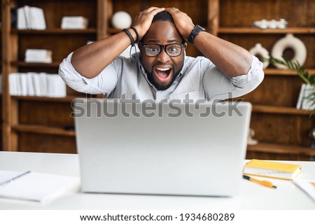 Shocked man is staring on the laptop screen, holding head and yelling happily, surprised African-American businessman received good news, won in lottery, male jobseeker get an unbelievable opportunity Royalty-Free Stock Photo #1934680289