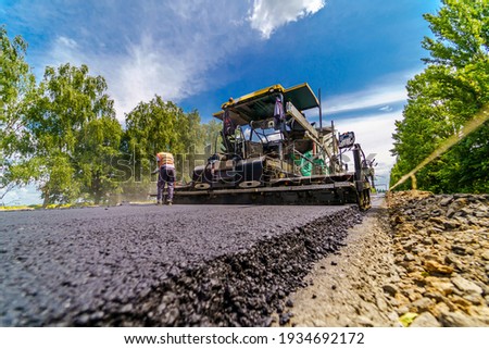 Road repair, compactor lays asphalt. Heavy special machines. Asphalt paver in operation. View from below. Closeup. Royalty-Free Stock Photo #1934692172