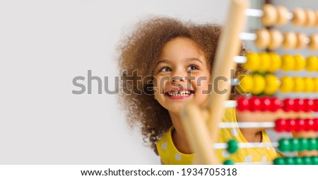 A Black student in a yellow dress laughs brightly behind a colored abacus in an elementary school classroom Royalty-Free Stock Photo #1934705318