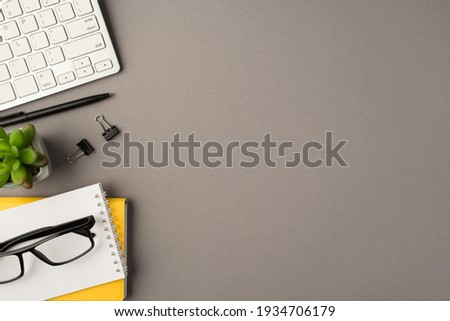 Above photo of notebook black pen paperclips keyboard plant and glasses isolated on the grey background with empty space
