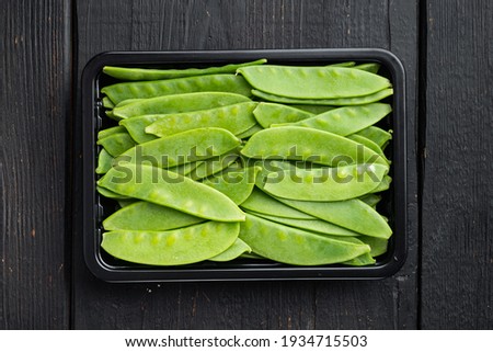 Sugar snap peas, raw ripe baby pods set, in plastic container, on black wooden background, top view flat lay Royalty-Free Stock Photo #1934715503