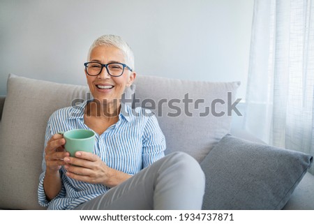 Happy lady relaxing at home with hot drink. Shot of a happy mature woman relaxing on the sofa with a warm beverage at home. Senior woman drinking hot drink sitting on sofa Royalty-Free Stock Photo #1934737871