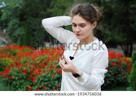 Young woman in white blouse wants to fix hairstyle on head, summer day in park close-up