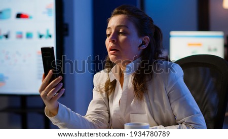 Entrepreneur having virtual meeting using smartphone with wireless headphone sitting at desk in workplace. Freelancer working with remotely team chatting virtual online conference, using internet