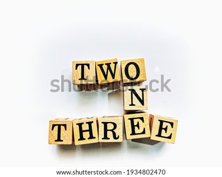 Close-up top view image of square wooden blocks crossword with the words, ONE TWO THREE on a white paper sheet background for decorative design.