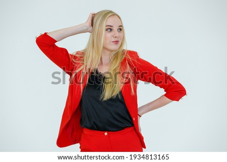Indoor portrait of young cute blond hair woman in red clothes poses to camera in advertising gesture with cheerful and positive emotion isolated on white background.