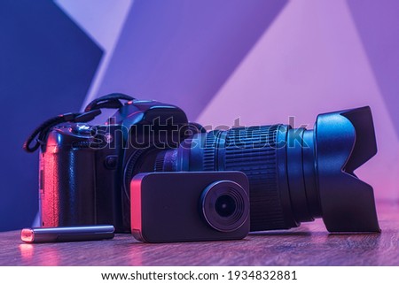 Set of equipment for photography and video filming. Photo camera with lens, action camera and usb flash drive on a wooden table in a studio with creative light.