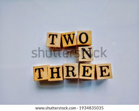 Close-up top view photo of square wooden blocks crossword with the words, TWO ONE THREE on a light gray paper sheet background for decorative design.