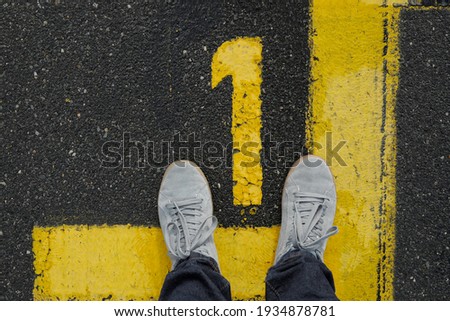 Men with grey sneker and jeans stand on the number 1, sign on the asphalt, yellow painted number and lines on dark street, space for text