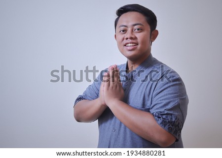 Portrait of religious Asian man in blue koko muslim shirt, showing apologize and welcome hand gesture. Isolated image over gray background