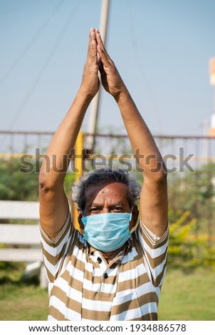 Old man with medical face mask busy doing surya namaskara yoga or exercise during morning - concept of senior people fitness workout and healthcare during coronavirus coivd-19 pandemic. Royalty-Free Stock Photo #1934886578