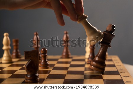 Queen beating king on chessboard. Checkmate in chess. Female hands and dark gray background.