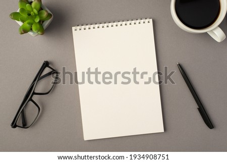 Above photo of notebook green plant glasses cup of coffee and black pen isolated on the grey background