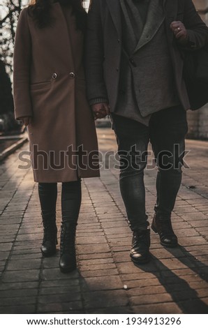 A couple, man and woman, walking on the winter street holding their hands toghether, feet, shoes and shadows