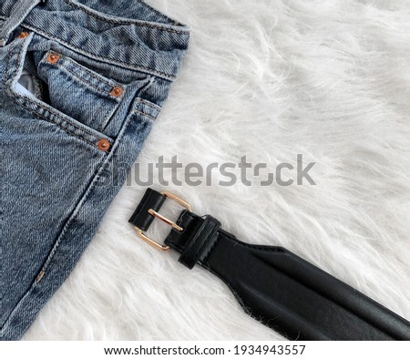 Women's black leather belt with a golden plate on a background of white fur close-up