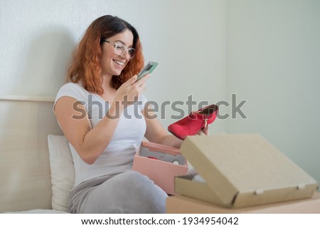 The woman unpacks the delivered shoes. The girl leaves a review about the order in the application on the smartphone