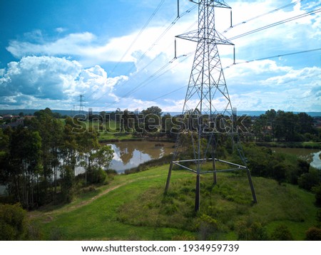 Aerial photo of overland power line tower structure, green grass, brown murky wetland lake, blue sky and white clouds