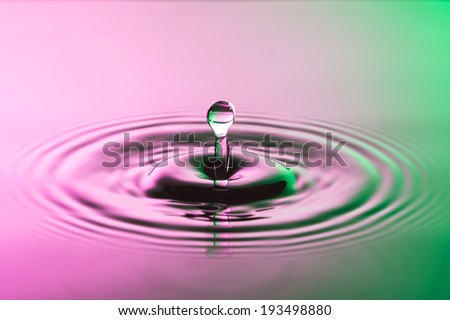 Water drop close up with concentric ripples on colourful pink and green surface