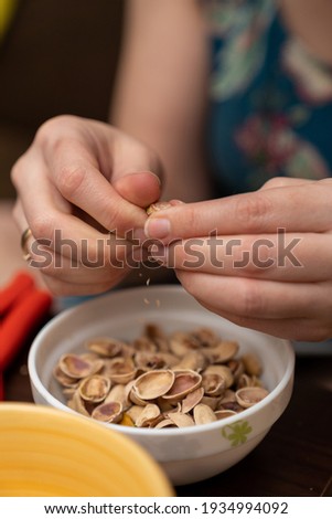 pistachios nuts in women's hand above the cup, pistachio shells visible in the cup.