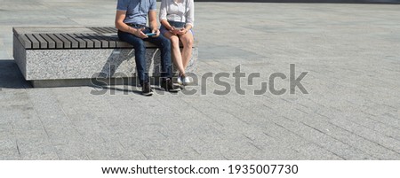 Two people sitting on a bench in the city are using their mobile phones