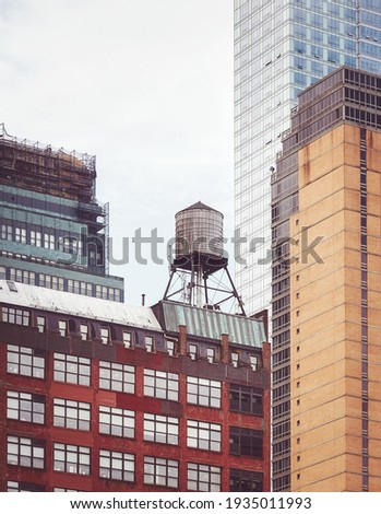 Old water tower, one of New York City symbols, among modern buildings, color toning applied, USA.