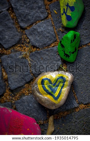 A blue heart with yellow background painted on a small stone und the ground. 