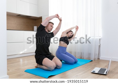 Young couple man and woman doing fitness at home online using laptop, doing online with trainer on floor at home sports Royalty-Free Stock Photo #1935015119