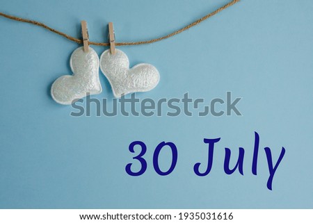 Commemorative date July 30 on blue background with white hearts with clothespins, flat lay. Holiday calendar concept International Day of Friendship