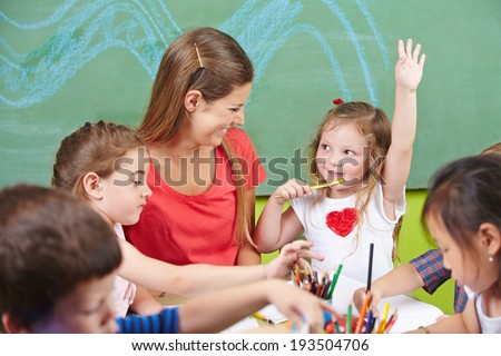 Girl raising her hand in preschool with painting a picture